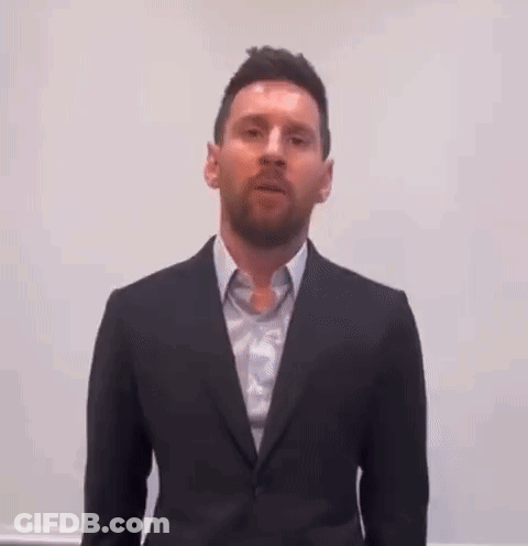 A Man Wearing A Suit And Tie Is Standing In Front Of A White Wall . GIF