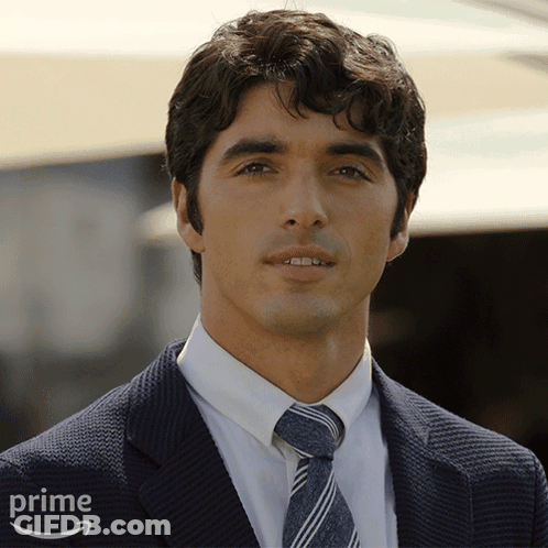 A Man Wearing A Suit And Tie Is Standing In Front Of An Amazon Prime Logo GIF