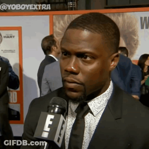 A Man Wearing A Suit And Tie Is Talking Into A Microphone With The Letters E On It GIF