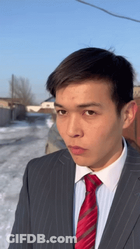 A Man Wearing A Suit And Tie Looks At The Camera GIF