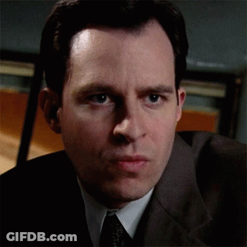 A Man Wearing A Suit And Tie Looks At The Camera GIF