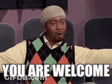 A Man Wearing A Sweater And A Hat Is Sitting In A Theater . GIF
