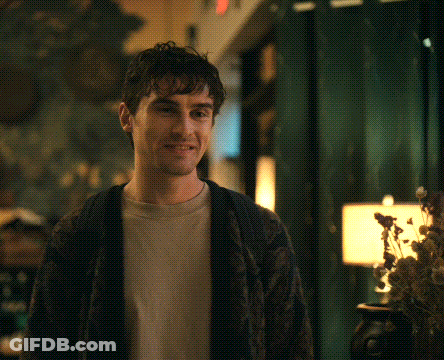 A Man Wearing A Sweater And A T-Shirt Is Smiling GIF