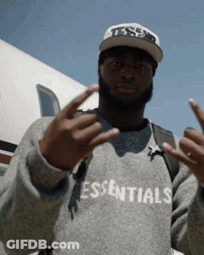 A Man Wearing A Sweater That Says Essentials Giving The Middle Finger GIF
