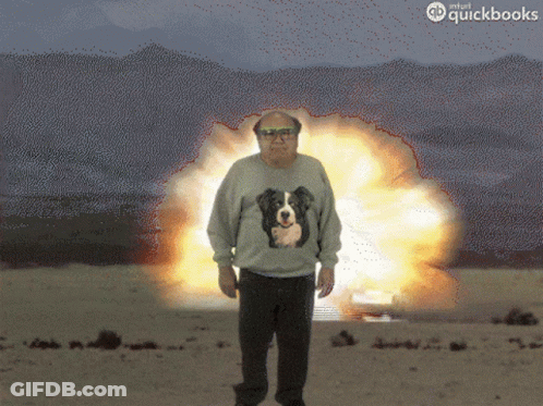 A Man Wearing A Sweater With A Dog On It Stands In Front Of An Explosion Sponsored By Quickbooks GIF