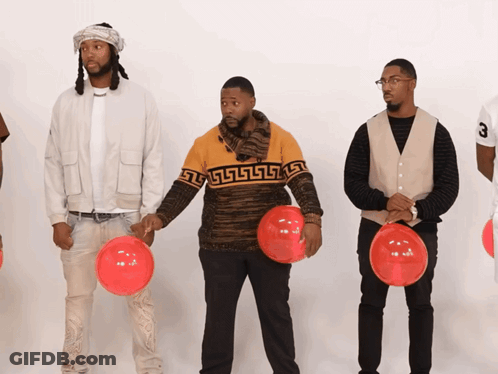 A Man Wearing A Sweater With A Greek Key Design Holds A Red Balloon GIF