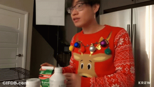 A Man Wearing A Sweater With A Reindeer On It Is Standing In Front Of A Refrigerator GIF