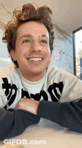 A Man Wearing A Sweatshirt That Says ' Thrasher ' On It Is Smiling While Sitting At A Table . GIF