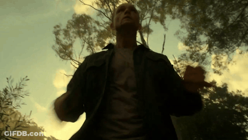 A Man Wearing A T-Shirt That Says ' A ' On It Stands In Front Of Trees GIF