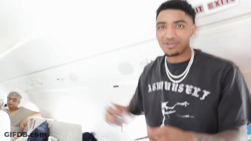 A Man Wearing A T-Shirt That Says Ashbury Is Standing In Front Of An Exit Sign . GIF