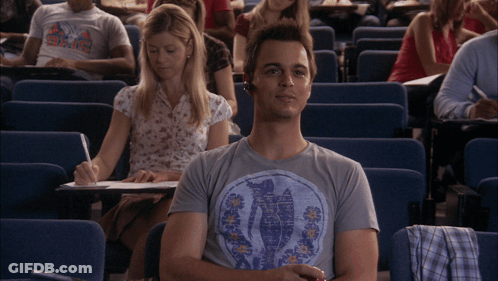 A Man Wearing A T-Shirt That Says ' Hawaii ' On It Sits In A Lecture Hall With Other Students GIF