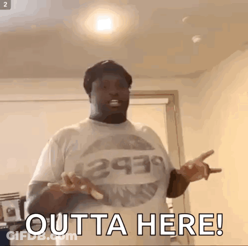 A Man Wearing A T-Shirt That Says Outta Here Is Standing In A Room With His Hands Outstretched . GIF