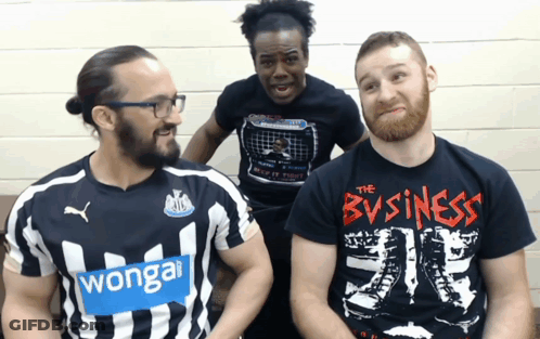 A Man Wearing A T-Shirt That Says The Business Sits Next To Two Other Men GIF