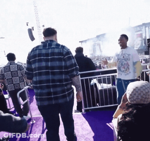 A Man Wearing A T-Shirt With A Dog On It Stands In A Crowd Of People GIF