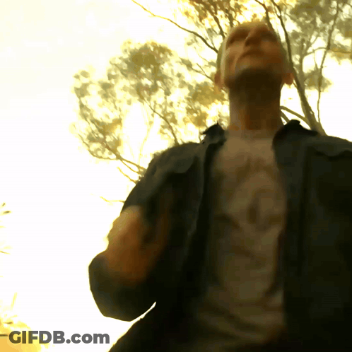A Man Wearing A T-Shirt With A Skull On It Stands In Front Of Trees GIF