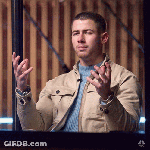 A Man Wearing A Tan Jacket And A Blue Sweater Is Holding His Hands Up In The Air GIF