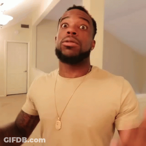 A Man Wearing A Tan T-Shirt And A Gold Necklace With A Dog Tag On It Looks Surprised GIF