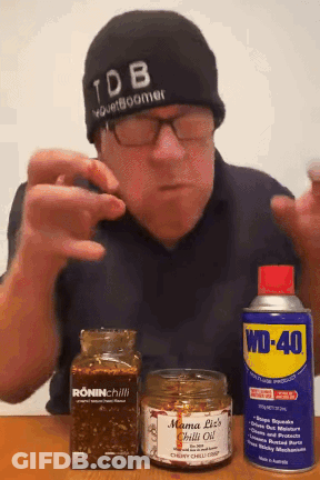 A Man Wearing A Tdb Hat Holds A Can Of Wd-40 And A Jar Of Mama Liz 'S Chilli Oil GIF
