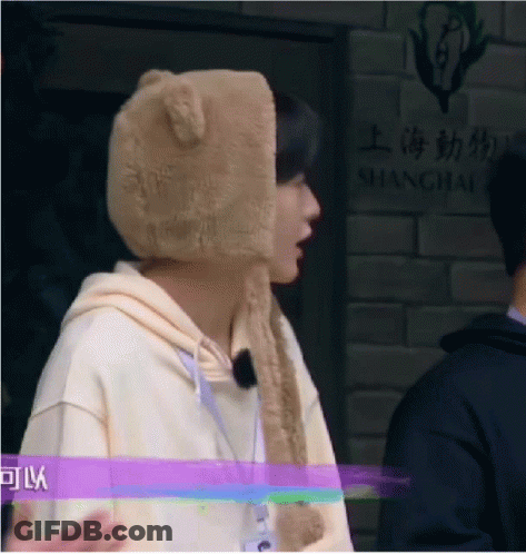A Man Wearing A Teddy Bear Hat Is Standing In Front Of A Shanghai Sign . GIF