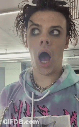 A Man Wearing A Tie Dye Hoodie With A Cat On It Makes A Funny Face GIF