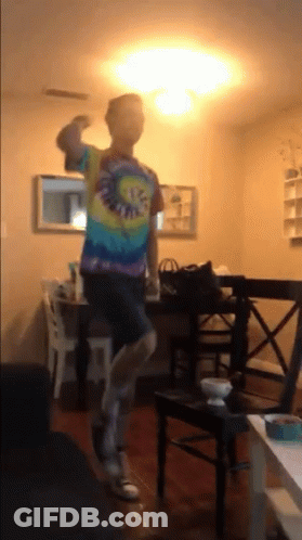 A Man Wearing A Tie Dye Shirt Is Dancing In A Living Room GIF