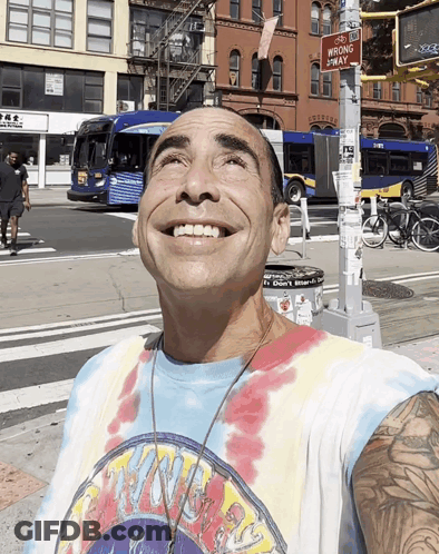 A Man Wearing A Tie Dye Shirt Is Smiling In Front Of A Sign That Says No Wrong Way GIF