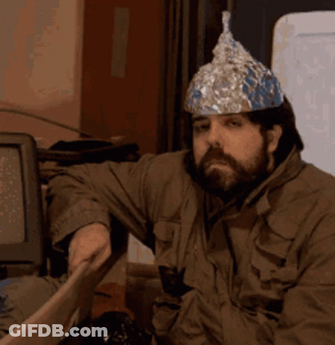 A Man Wearing A Tin Foil Hat Sits In Front Of A Computer Monitor GIF