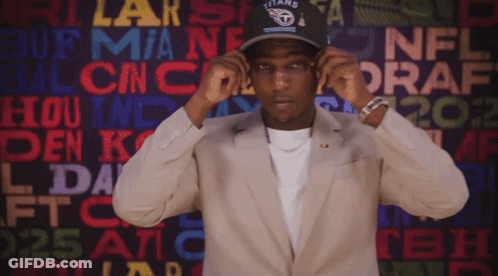 A Man Wearing A Titans Hat Stands In Front Of A Wall Of Nfl Draft Logos GIF