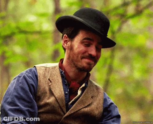 A Man Wearing A Top Hat And A Vest Smiles In Front Of Trees GIF