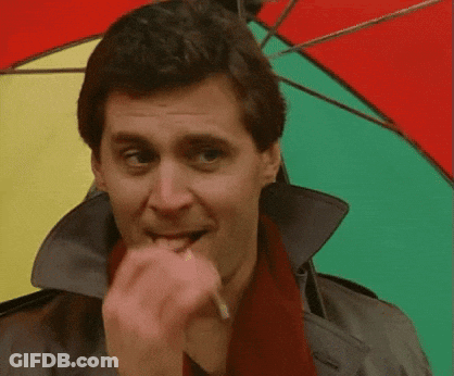 A Man Wearing A Trench Coat And Scarf Is Biting A Cigarette While Holding A Colorful Umbrella GIF