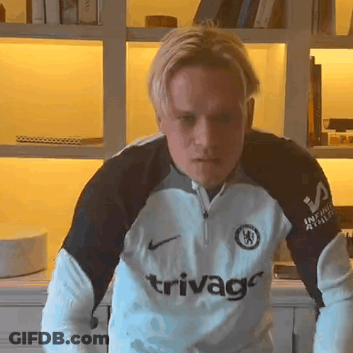 A Man Wearing A Trivago Jersey Stands In Front Of A Bookshelf GIF