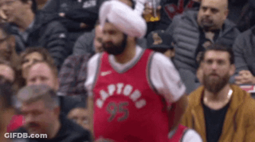 A Man Wearing A Turban And A Raptors Jersey Sits In The Crowd GIF