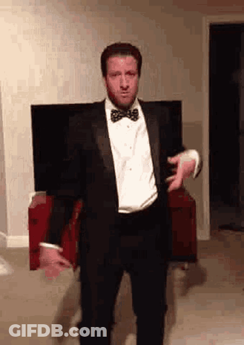 A Man Wearing A Tuxedo And Bow Tie Is Dancing In A Living Room . GIF