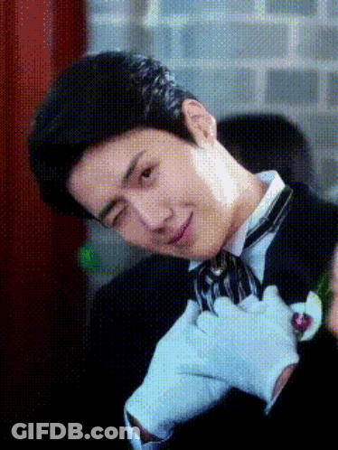 A Man Wearing A Tuxedo And White Gloves Is Making A Face GIF