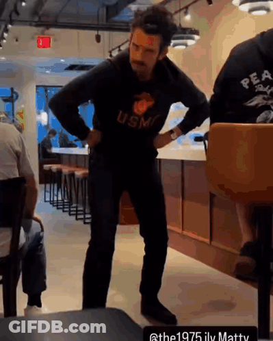 A Man Wearing A Usmc Sweatshirt Stands In A Restaurant GIF
