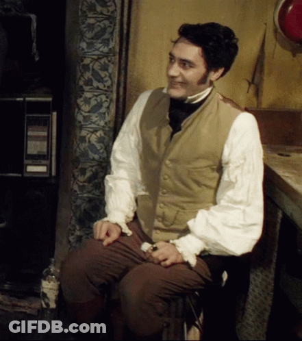A Man Wearing A Vest And A White Shirt Is Sitting On A Chair GIF