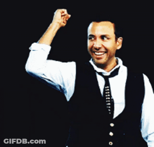 A Man Wearing A Vest And Tie Holds His Fist Up In The Air GIF
