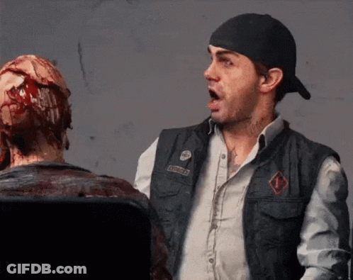 A Man Wearing A Vest With A Patch That Says ' Apocalypse ' On It Stands Next To A Bloody Statue GIF