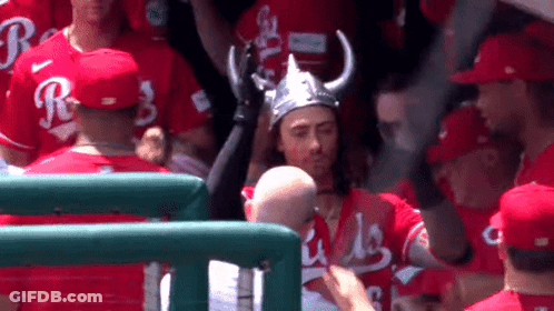A Man Wearing A Viking Hat Stands In A Crowd Of Baseball Players Wearing Red Jerseys With The Letter R On Them GIF