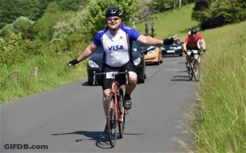 A Man Wearing A Visa Shirt Is Riding A Bike Down A Road GIF