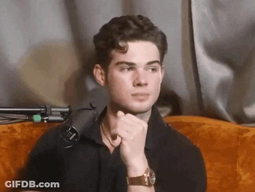 A Man Wearing A Watch Is Sitting In Front Of A Microphone With The Letter L On It GIF