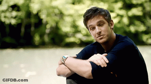 A Man Wearing A Watch Sits With His Arms Crossed In Front Of Trees GIF