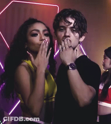 A Man Wearing A Watch Stands Next To A Woman Who Is Covering Her Mouth With Her Hand GIF