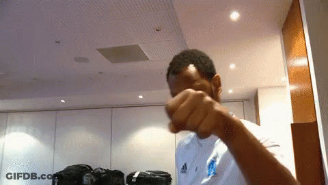 A Man Wearing A White Adidas Shirt Holds His Fist Up GIF