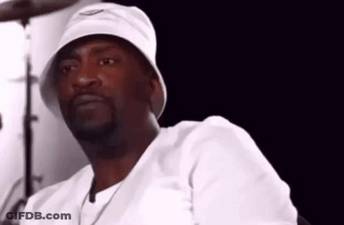 A Man Wearing A White Bucket Hat And A White Shirt Is Sitting In Front Of A Drum Set . GIF