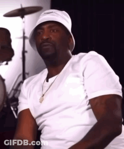 A Man Wearing A White Bucket Hat And A White Shirt Is Sitting In Front Of A Drum Set . GIF