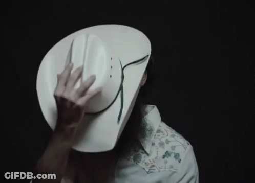 A Man Wearing A White Cowboy Hat Is Covering His Face With It GIF