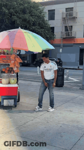 A Man Wearing A White Emirates Shirt Stands In Front Of A Cart GIF