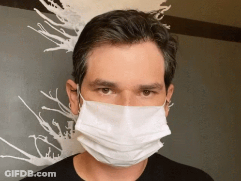 A Man Wearing A White Face Mask Stands In Front Of A Painting GIF