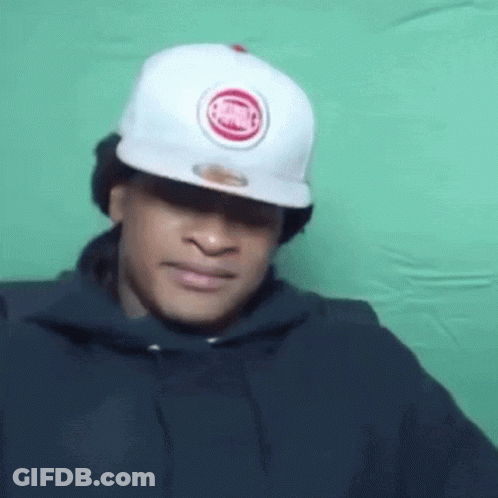 A Man Wearing A White Hat And A Black Hoodie Is Making A Face . GIF